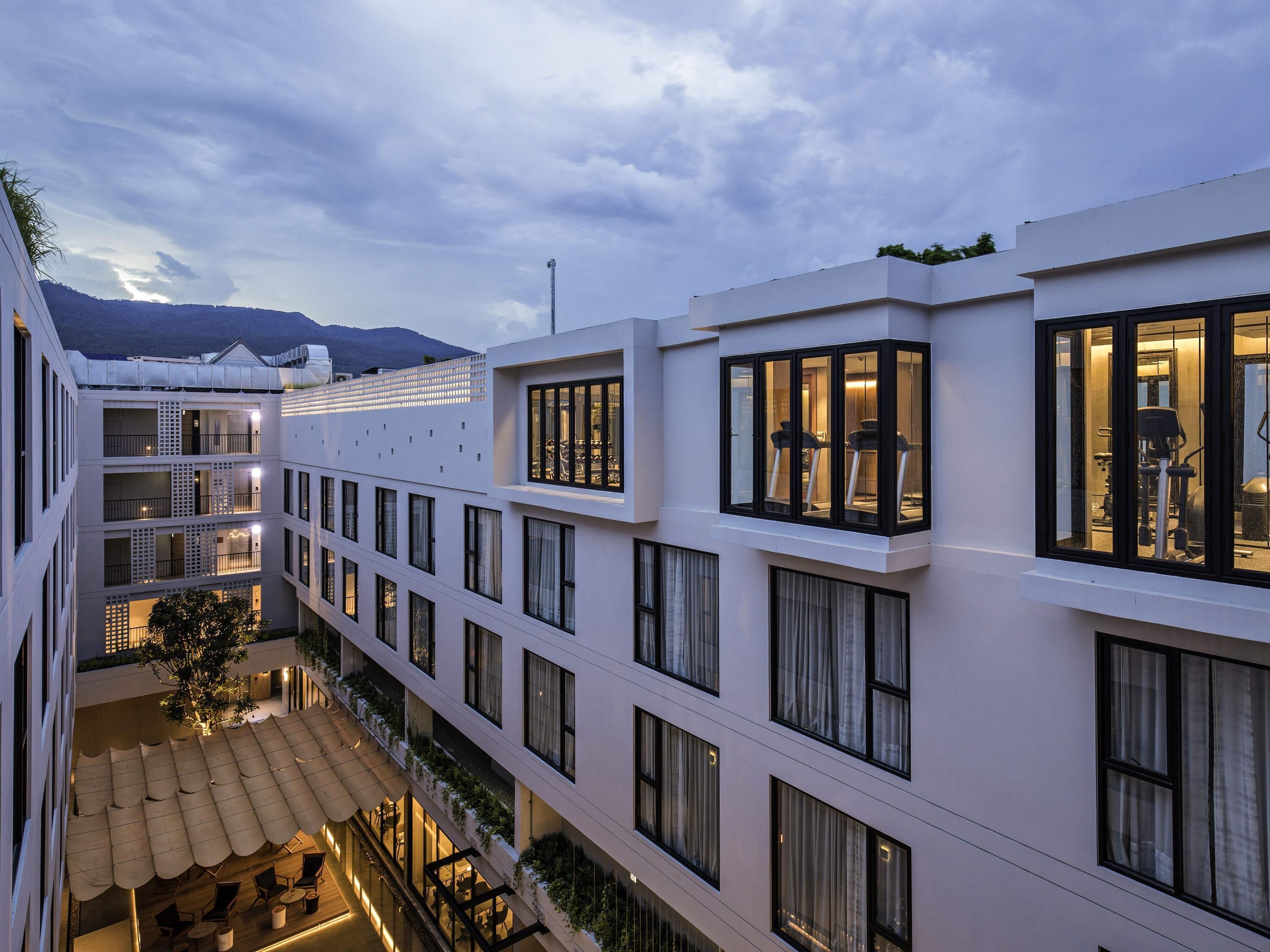 A multi-story hotel with balconies, outdoor seating, and a view of the mountains.