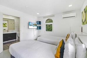 A modern bedroom with two beds, a TV, an air conditioning unit, and a window with a view of greenery.
