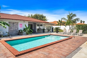 A swimming pool with a tiled deck, a covered patio area, and lounge chairs. - Prime Location: Spacious 4BR Home w/ Pool*Backyard (Noord)