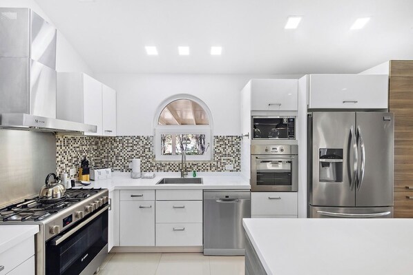 A modern kitchen with stainless steel appliances, white cabinetry, and a tiled backsplash.