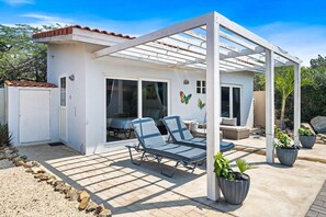 A covered outdoor area with two lounge chairs, a pergola, and potted plants.