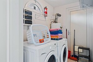 A laundry area with a washing machine, a dryer, a fire extinguisher, and a stack of folded clothes.
