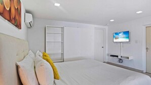Una camera d'albergo con un letto, una televisione montata a parete e un armadio bianco.