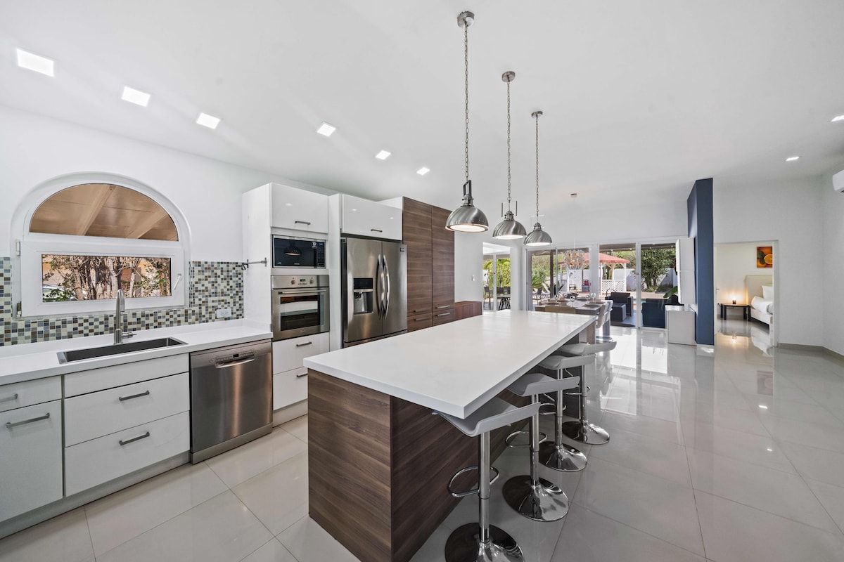 Una cocina moderna con una isla central, electrodomésticos de acero inoxidable e iluminación colgante.
