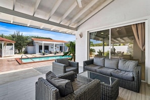 A covered outdoor area with wicker furniture, a pool, and a view of a house with a red roof. - Prime Location: Spacious 4BR Home w/ Pool*Backyard (Noord)