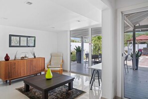 A modern living room with a wooden cabinet, a sofa, a coffee table, and a dining area with a table and chairs. - Spacious 4BR Home w/ Private Pool & Backyard (Noord)