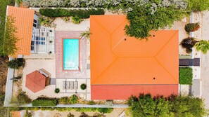 An aerial view of a property with a swimming pool, a covered patio, and a large orange-roofed area.