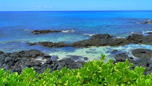 A coastal landscape with clear blue waters, rocky formations, and green vegetation.