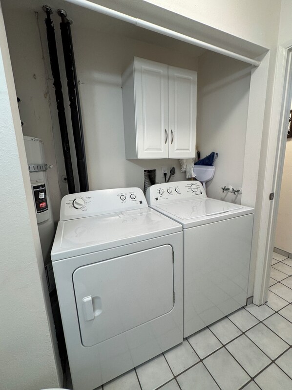 A laundry room with two front-loading washing machines, a white cabinet above, and a water heater to the left. - Tropical Paradise Awaits: Stunning Hawaii Condo with Ocean Views!
(Kailua-Kona)