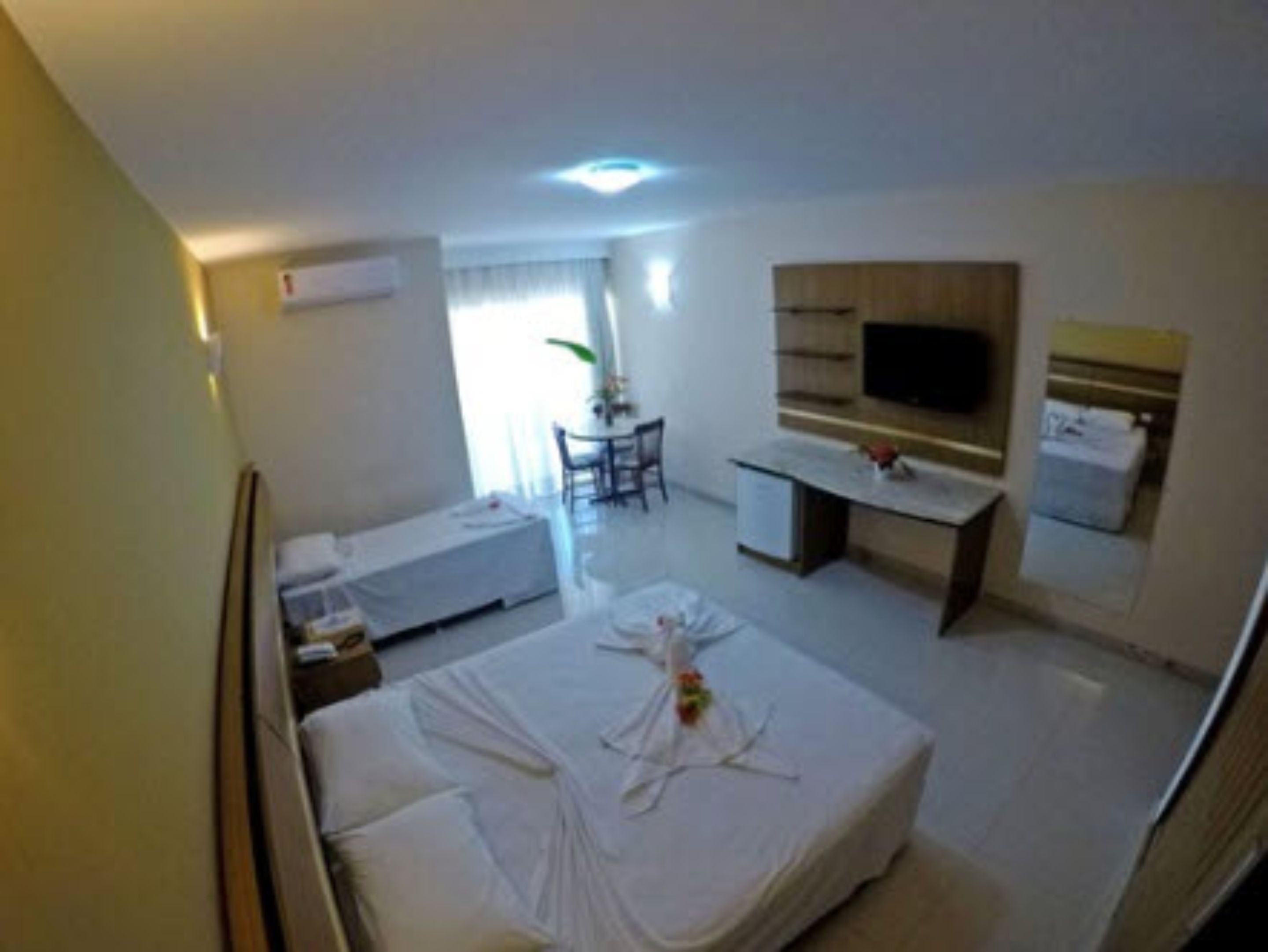 A hotel room with a bed, a desk, a chair, a TV, and a window.