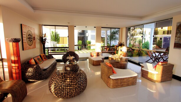 Un salón amplio con mobiliario de mimbre, ventanas grandes y vistas al jardín exterior.