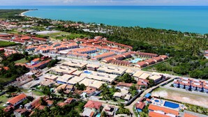 Vista aérea de un complejo turístico con varias edificaciones, una piscina y una playa al fondo.