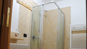 Un baño con ducha envuelta en vidrio, lavamanos, inodoro y toallero.