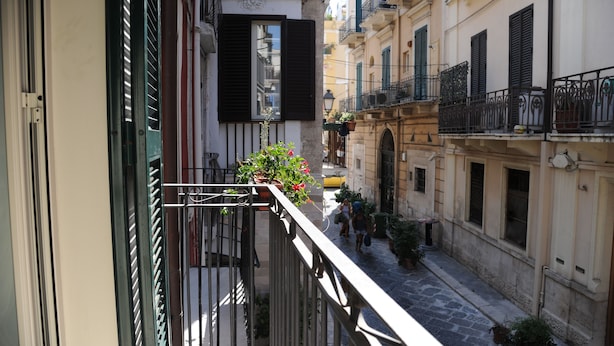 Una calle estrecha flanqueada por edificios, balcones con barandillas y plantas en macetas.