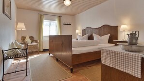 Une chambre avec un lit en bois, deux tables de chevet avec des lampes, une chaise en osier, une fenêtre avec des rideaux et un plafond en bois.