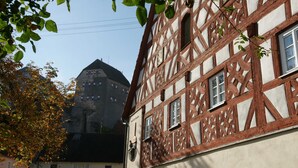 Un bâtiment à pans de bois, avec des encadrements de fenêtres apparents et une tour en pierre en arrière-plan.