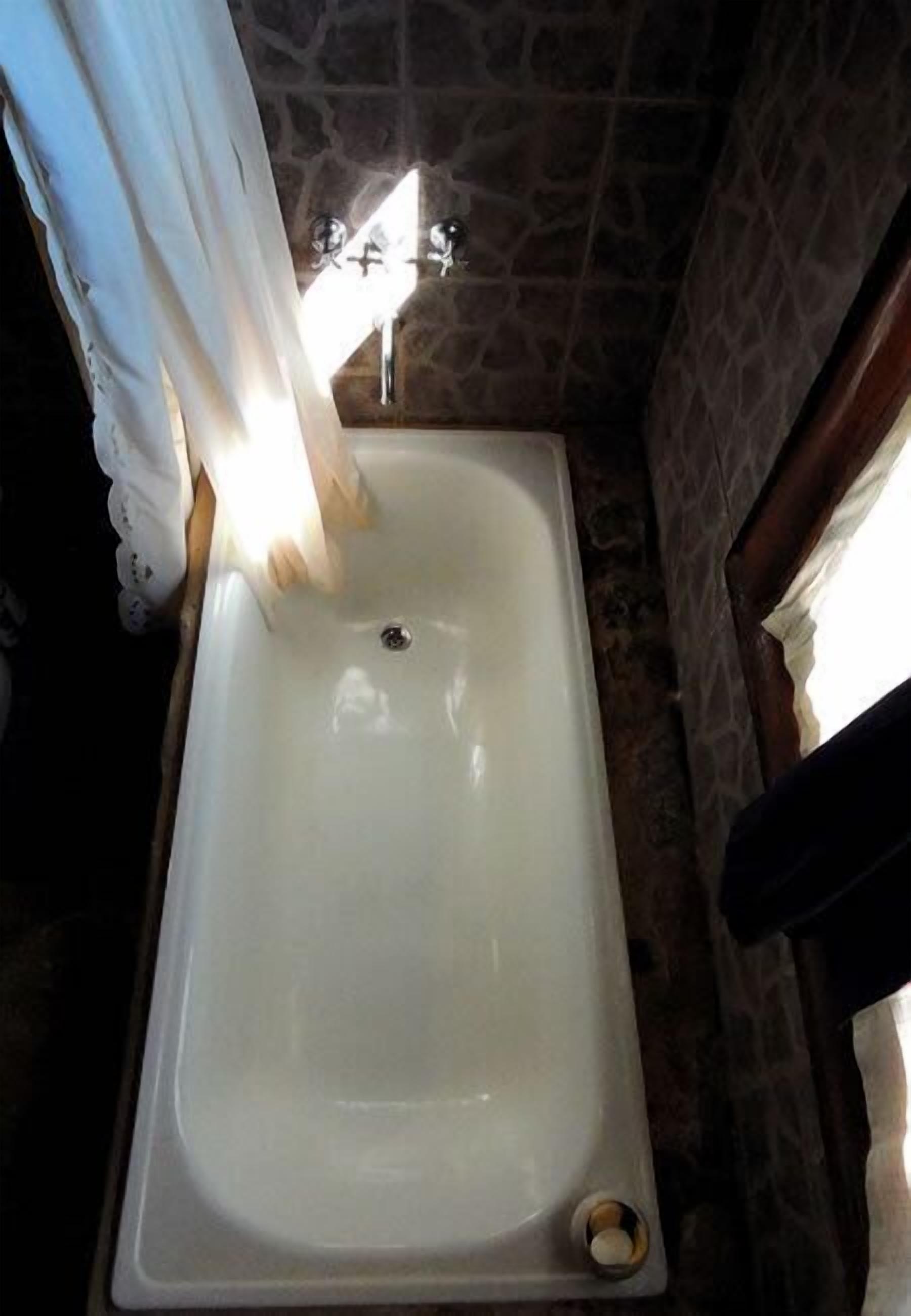 A rectangular bathtub with a drain, set against a stone wall.