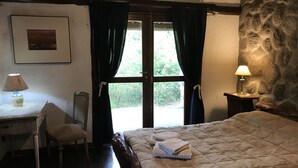 A bedroom with a bed, a desk, a chair, a lamp, and a stone wall.