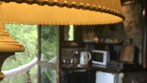 A close-up of a lamp with a scalloped edge, a window with a white curtain, and a kitchen area with a microwave and other appliances. - Cabanas Merlin (Merlo)