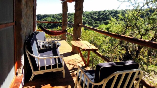 A wooden deck with a hammock, two lounge chairs, and a table overlooking a forested landscape. - Cabanas Merlin (Merlo)