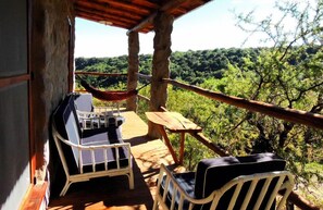 A wooden deck with a hammock, two lounge chairs, and a table overlooking a forested landscape. - Cabanas Merlin (Merlo)