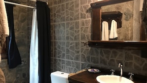 A bathroom with a stone wall, a white toilet, a wooden vanity with a sink, and a mirror.