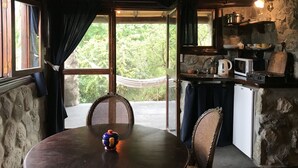 A rustic kitchen with a stone wall, wooden ceiling, and a view of greenery outside. - Cabanas Merlin (Merlo)