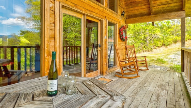 Un patio in legno con tavolo e sedie, una bottiglia di vino e una poltrona a dondolo.