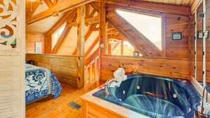 Interno di una baita in legno con una camera da letto, un bagno con vasca idromassaggio e un'ampia finestra a lucernario.