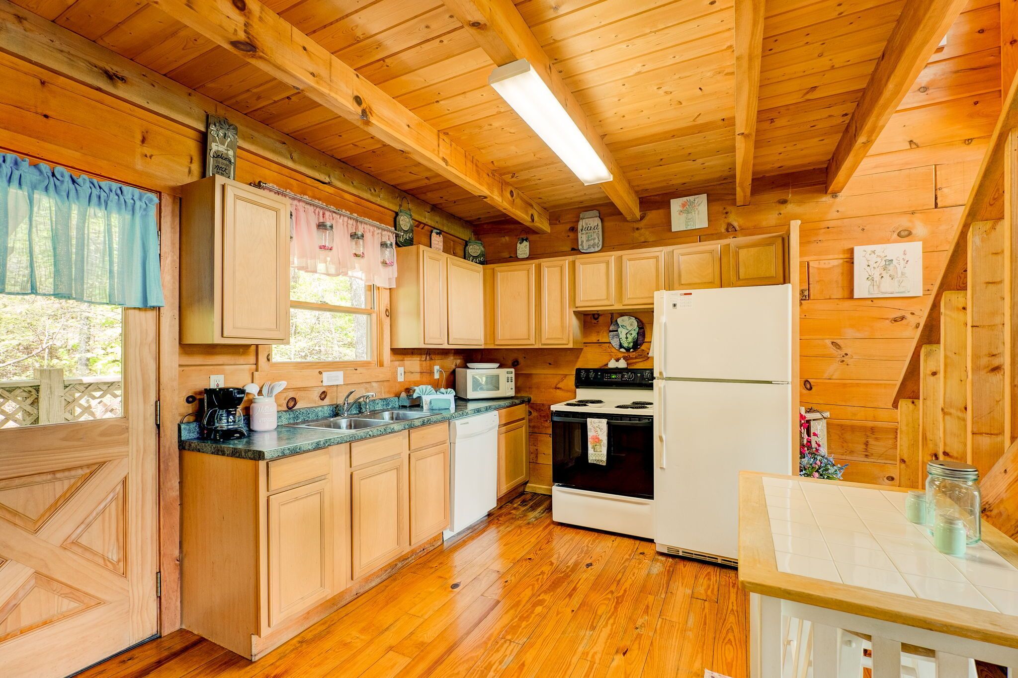 A wooden cabin kitchen with wooden cabinets, a microwave, a stove, and a refrigerator.