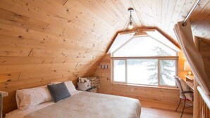 Een gezellig houten slaapkamer met een groot bed, een klein bureau en een raam met uitzicht op een besneeerd landschap.