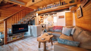 Een gezellig cabin interieur met een houten trap, een woonkamer met een leren bank, een salontafel en een tv waarop 'NETFLIX' staat.