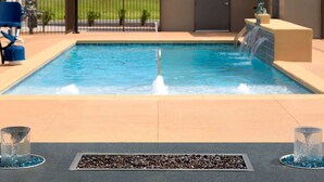 Ein Swimmingpool mit Wasserspiel, umgeben von einer Terrasse mit Sitzgelegenheiten und einem Ziergartenpflanzgefäß.