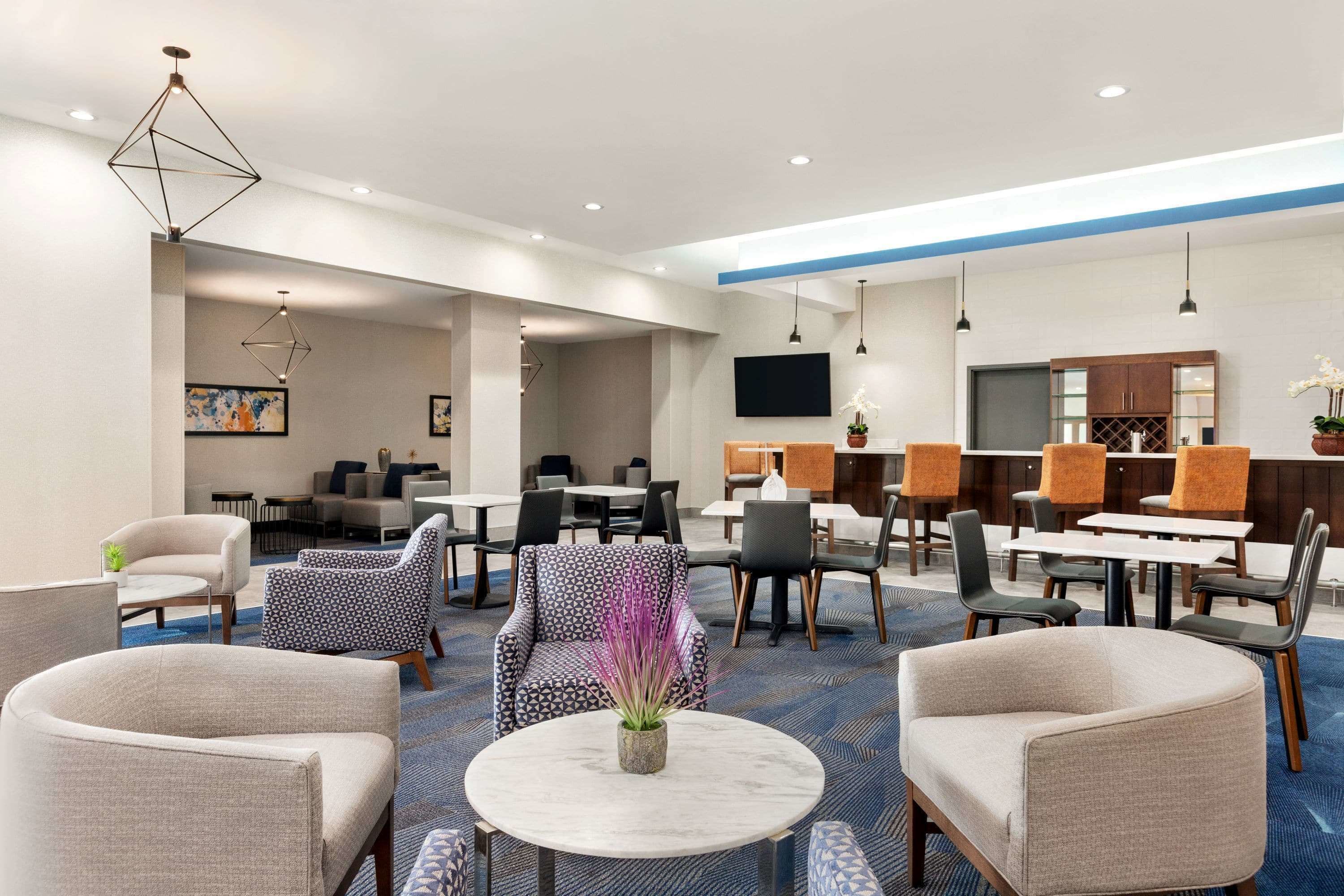 En modern hotellobby med en blandning av sittgrupper, ett stort runt bord i mitten och en platt-TV som är monterad på väggen.