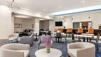 Un moderno vestíbulo de hotel con una variedad de zonas de estar, una mesa redonda central y un televisor de pantalla plana montado en la pared.