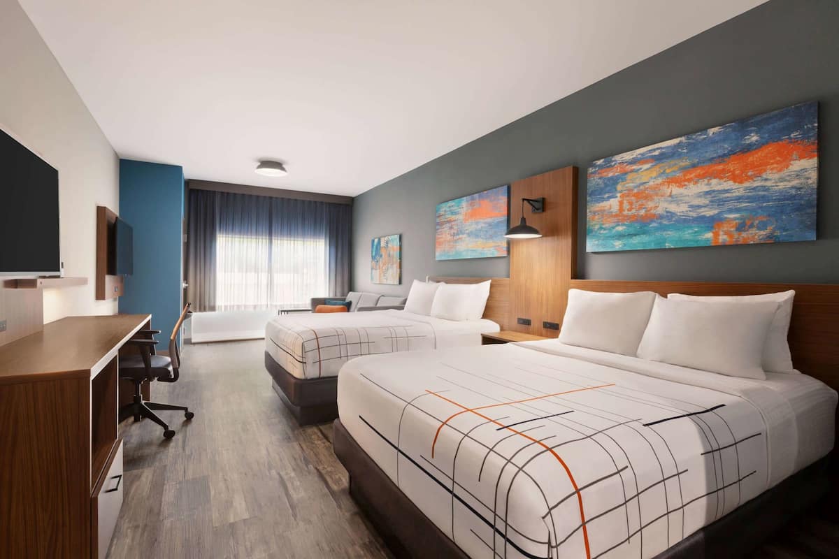 A modern hotel room with two beds, a desk, and a TV.