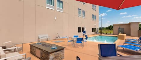 A poolside area with lounge chairs, a fire pit, and a swimming pool.