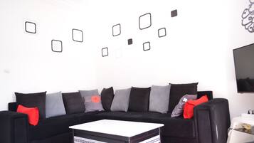 A modern living room with a black sofa, red and grey cushions, a white coffee table, and a wall with geometric wall art.