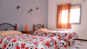 Een slaapkamer met twee bedden, een nachtkastje met een lamp, een raam met gordijnen, en decoratieve muurstickers.
