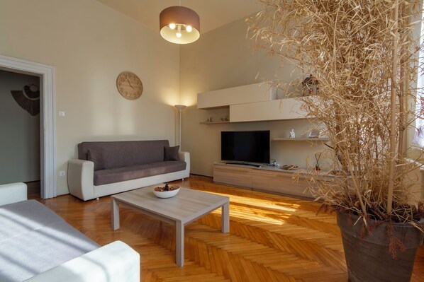 A modern living room with a sofa, coffee table, TV, and a potted plant.