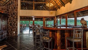 A bar area with stone walls, wooden ceiling, and a view of the outdoors. - Sekala Private Game Lodge (Vaalwater)