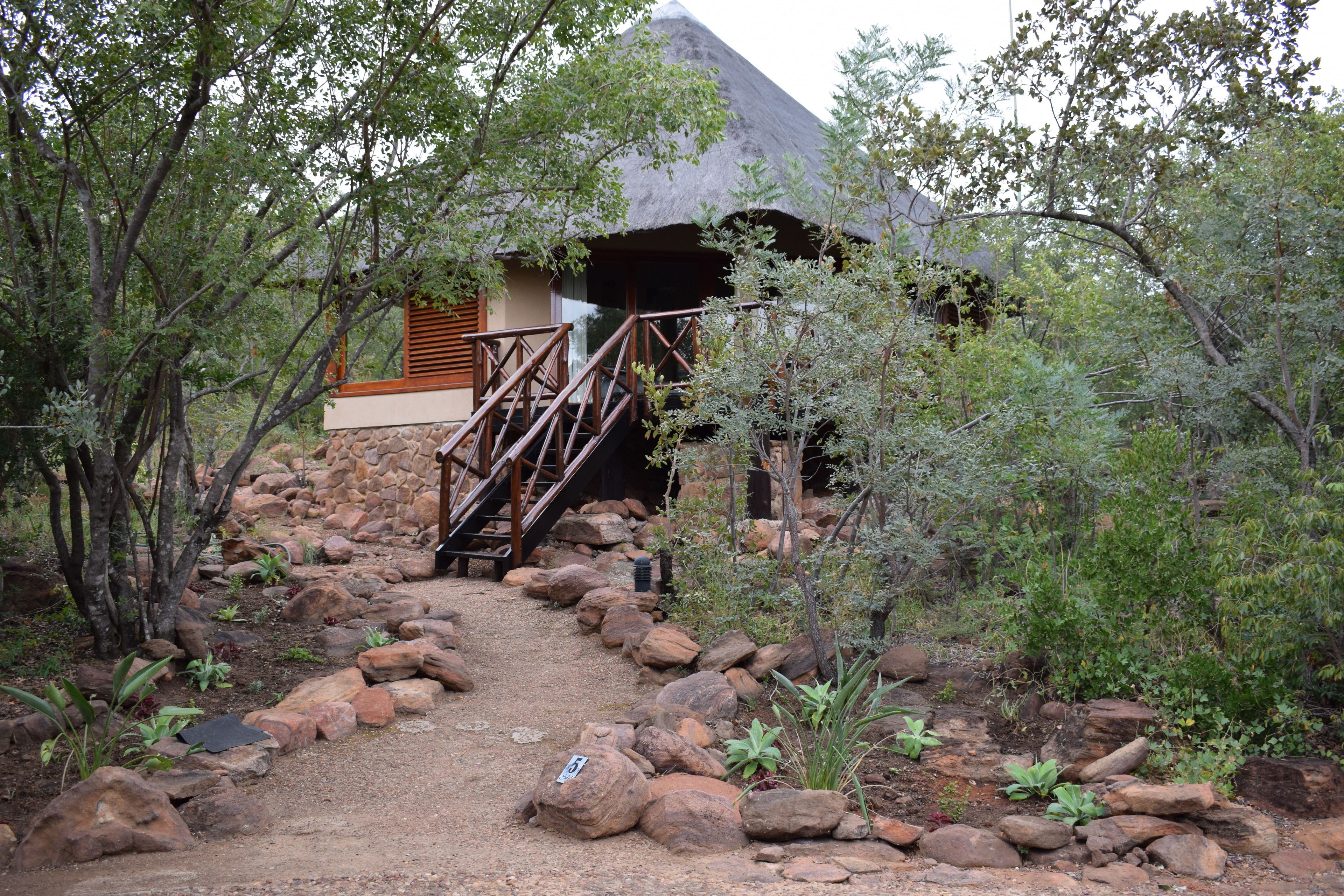 A pathway leading to a building with a thatched roof, surrounded by rocks and vegetation.