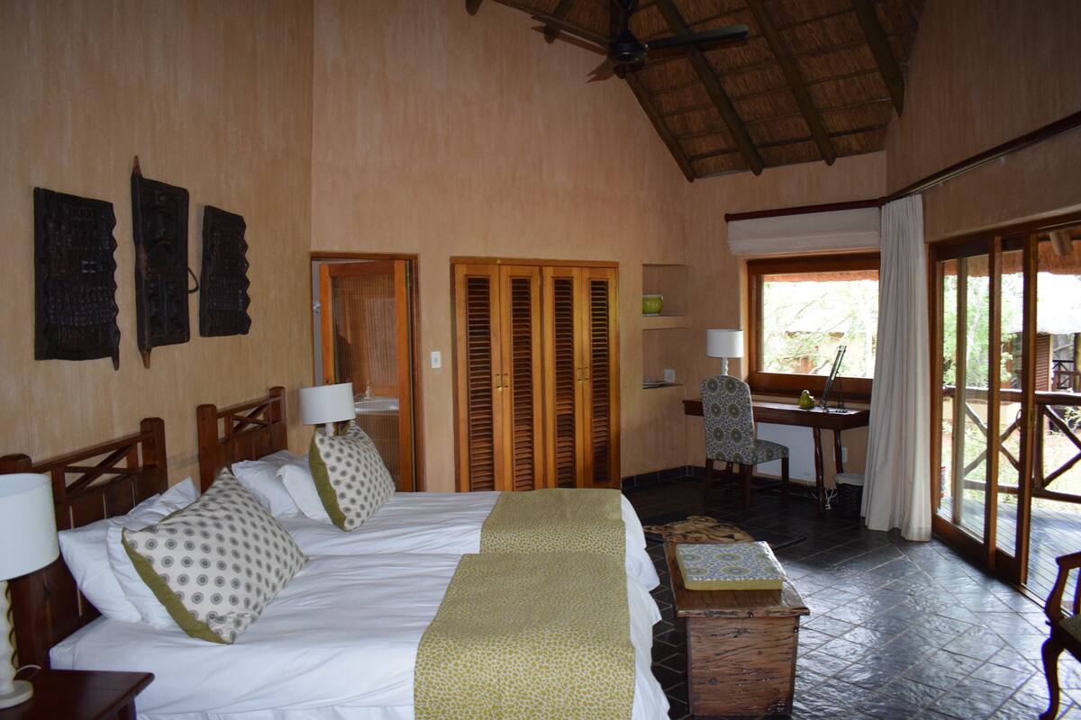 A hotel room with a large bed, two bedside tables, a chair, a small table, and a window with curtains.