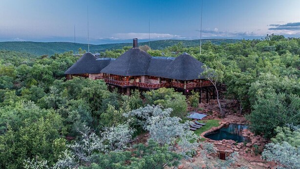 A thatched-roof house with a wooden deck, surrounded by dense greenery and a small pool. - Sekala Private Game Lodge (Vaalwater)