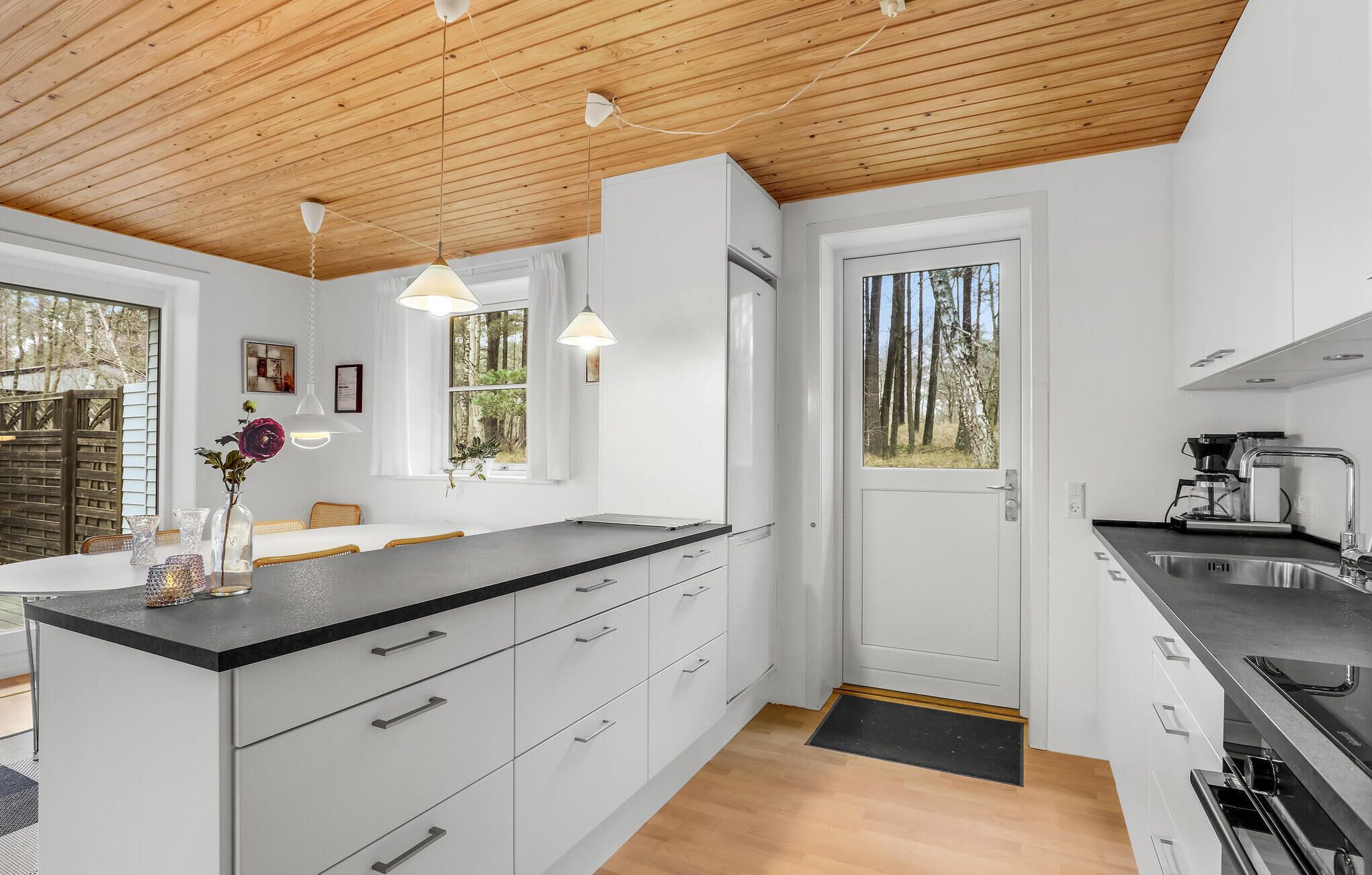 A modern kitchen with white cabinets, a black countertop, and wooden ceiling beams.