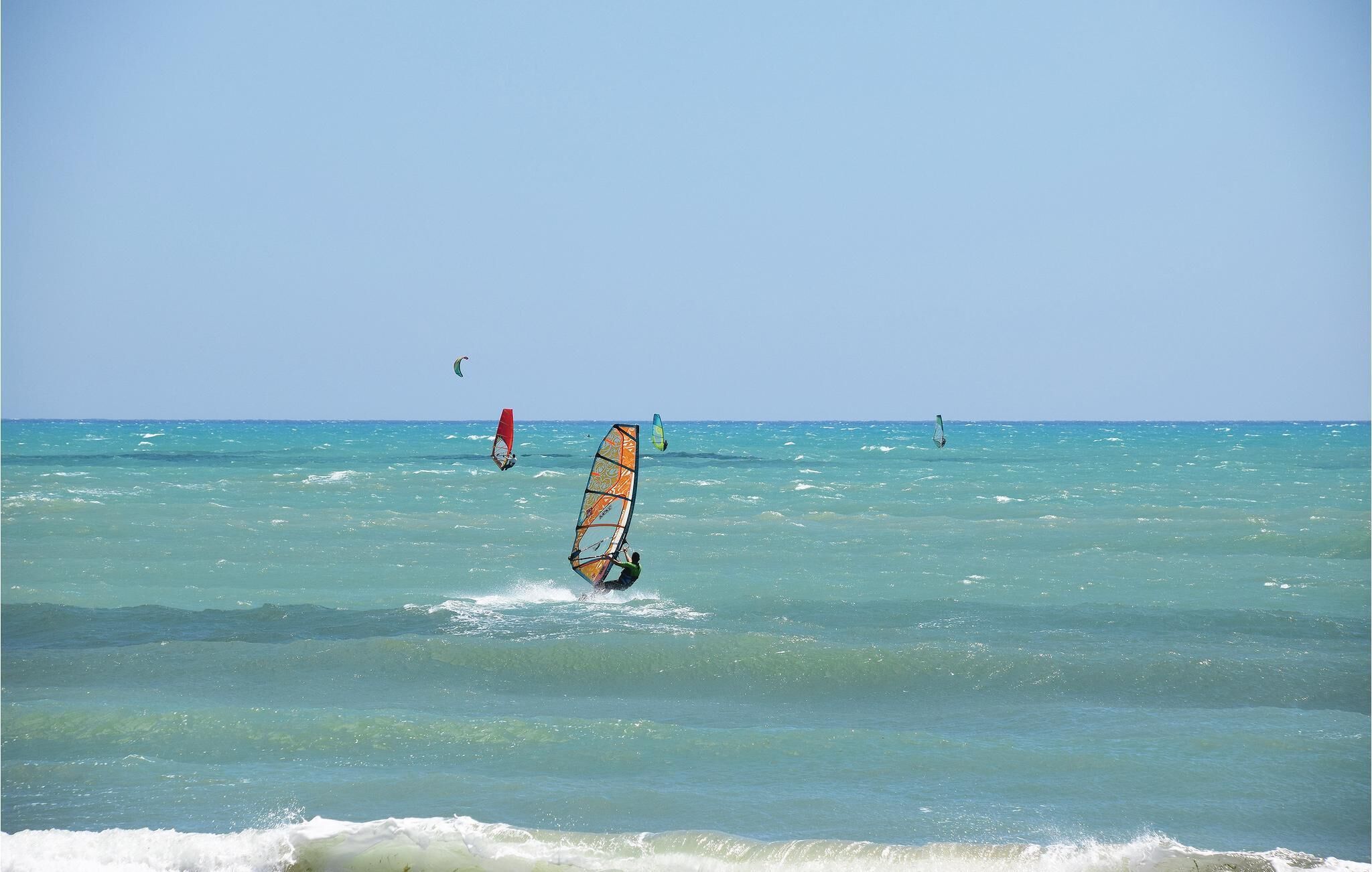 Une plage avec une eau turquoise et cristalline, et une personne pratiquant la planche à voile.