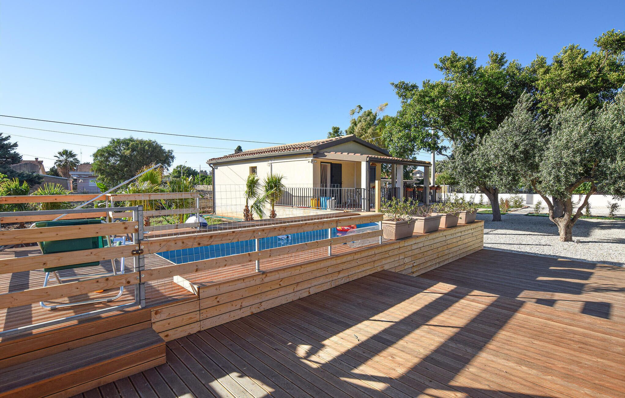 En træterrasse med en pool, en lille bygning med et tegltag og et træ.