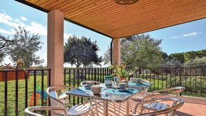 Een terras buiten met een ronde tafel en zes stoelen, omgeven door een houten pergola en een metalen hek.