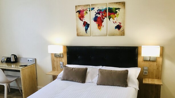 Ein Hotelzimmer mit einem großen Bett, zwei Nachttischen, einem Schreibtisch und einem Stuhl. An jedem Nachttisch befinden sich jeweils zwei Wandlampen.