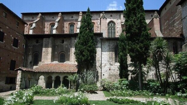 Ein Innenhof mit einem historischen Gebäude, das rundbogige Fenster und ein Ziegeldach zeigt.